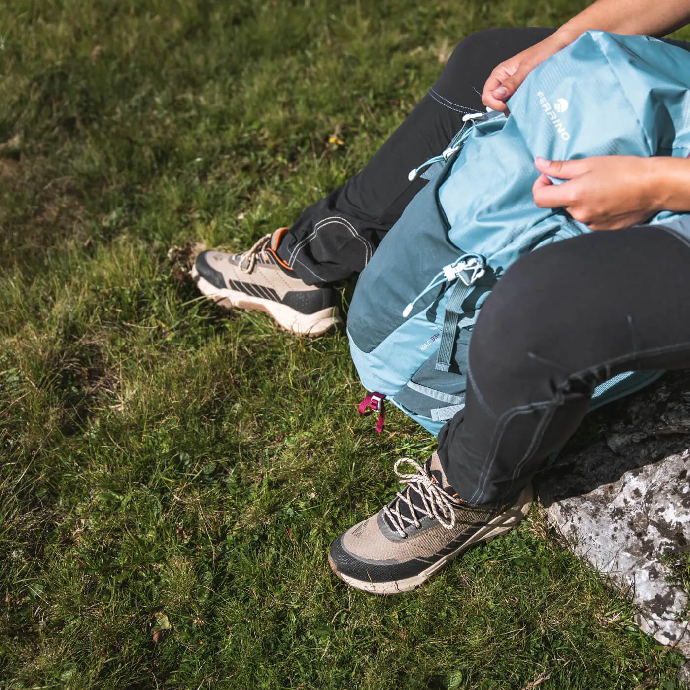 Person sitting on a rock with a blue backpack in a grassy area