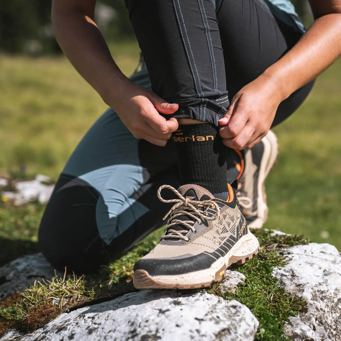 Person tying shoelaces on a hiking boot in a natural setting