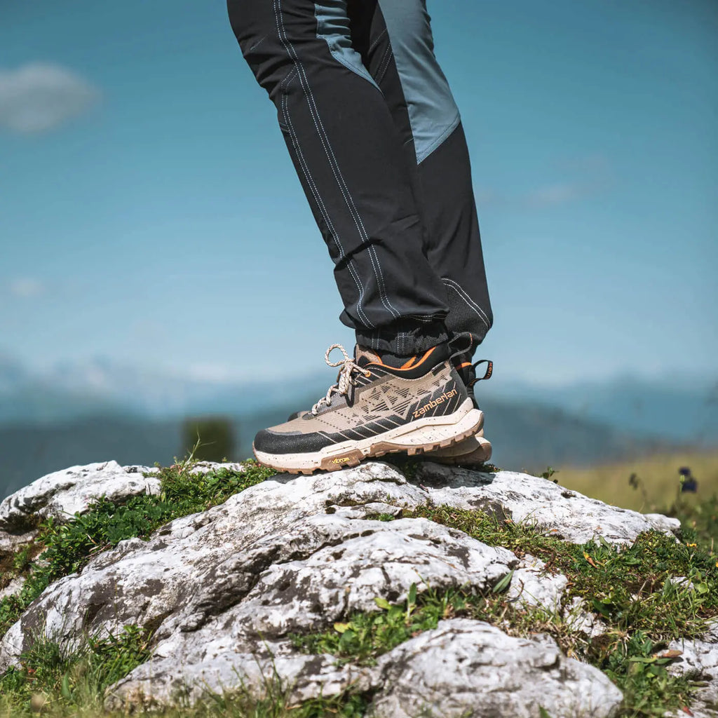 Person wearing hiking shoes and pants on a rocky mountain top with a clear sky.