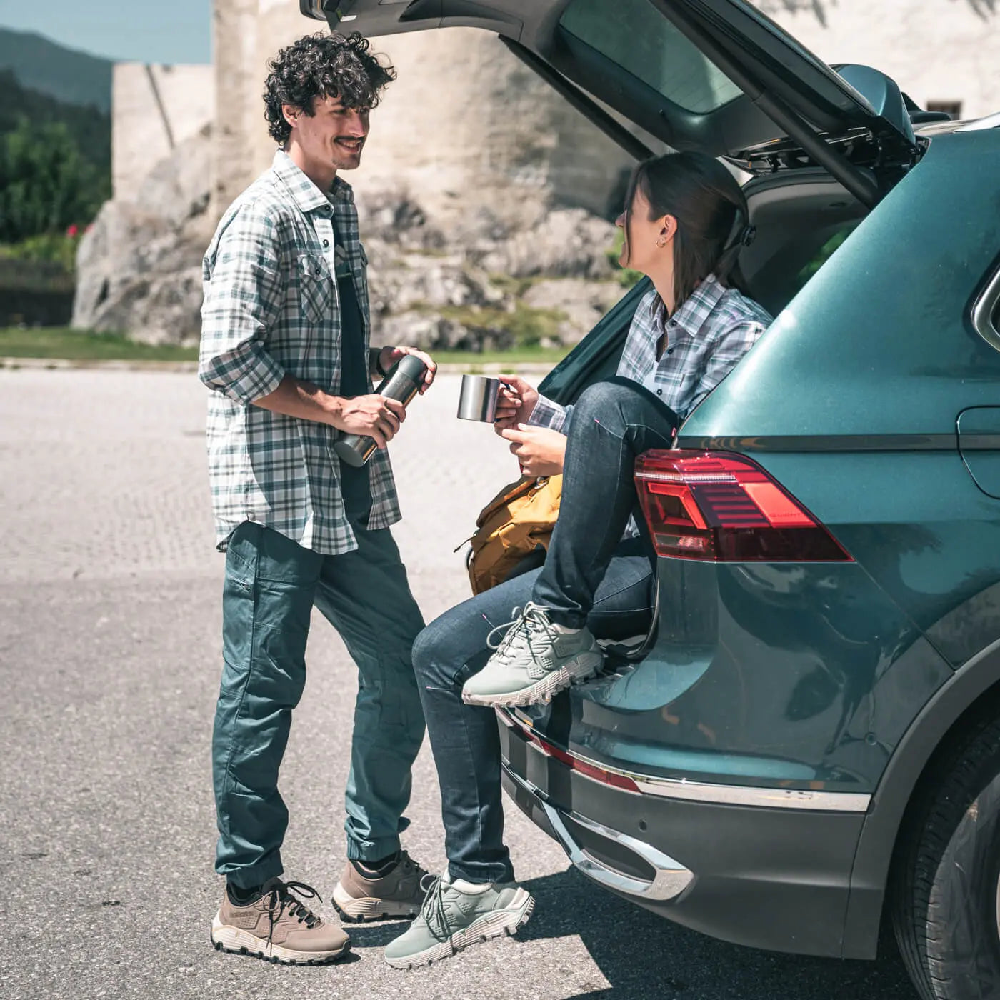Two men by a teal car with mountains in the background
