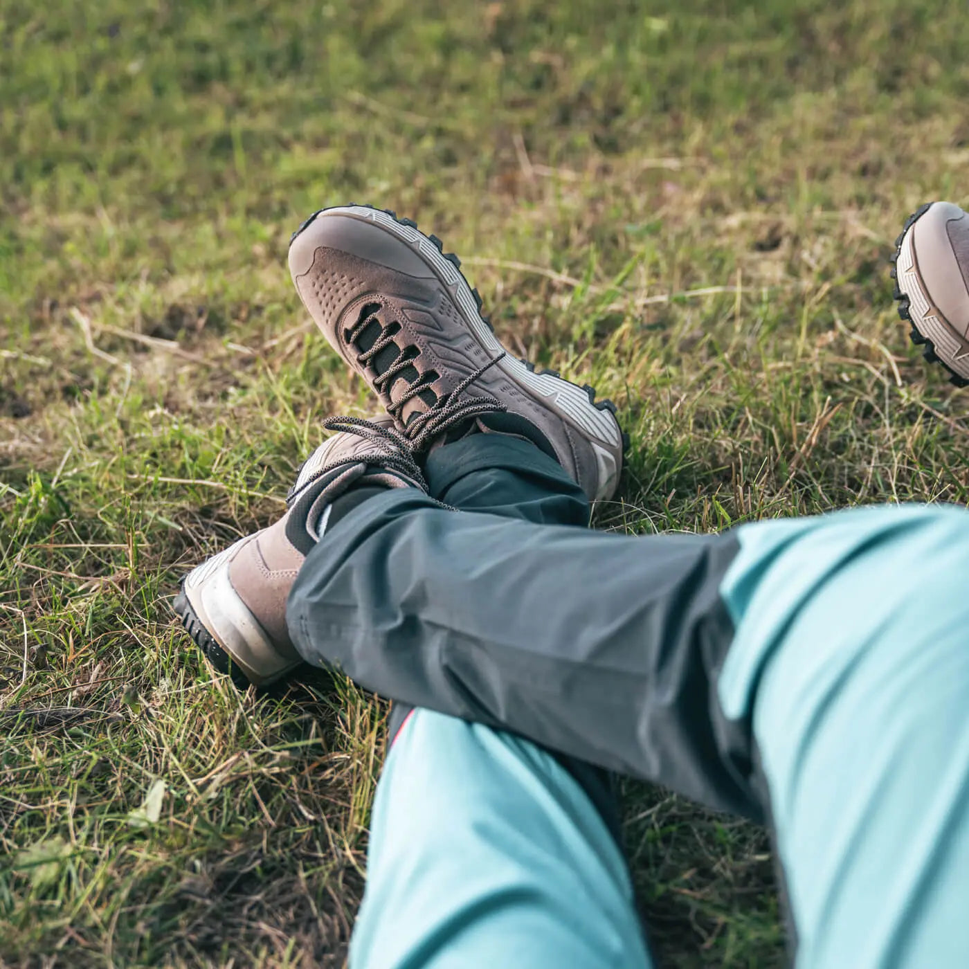 Person sitting on grass wearing beige sneakers and light blue pants.