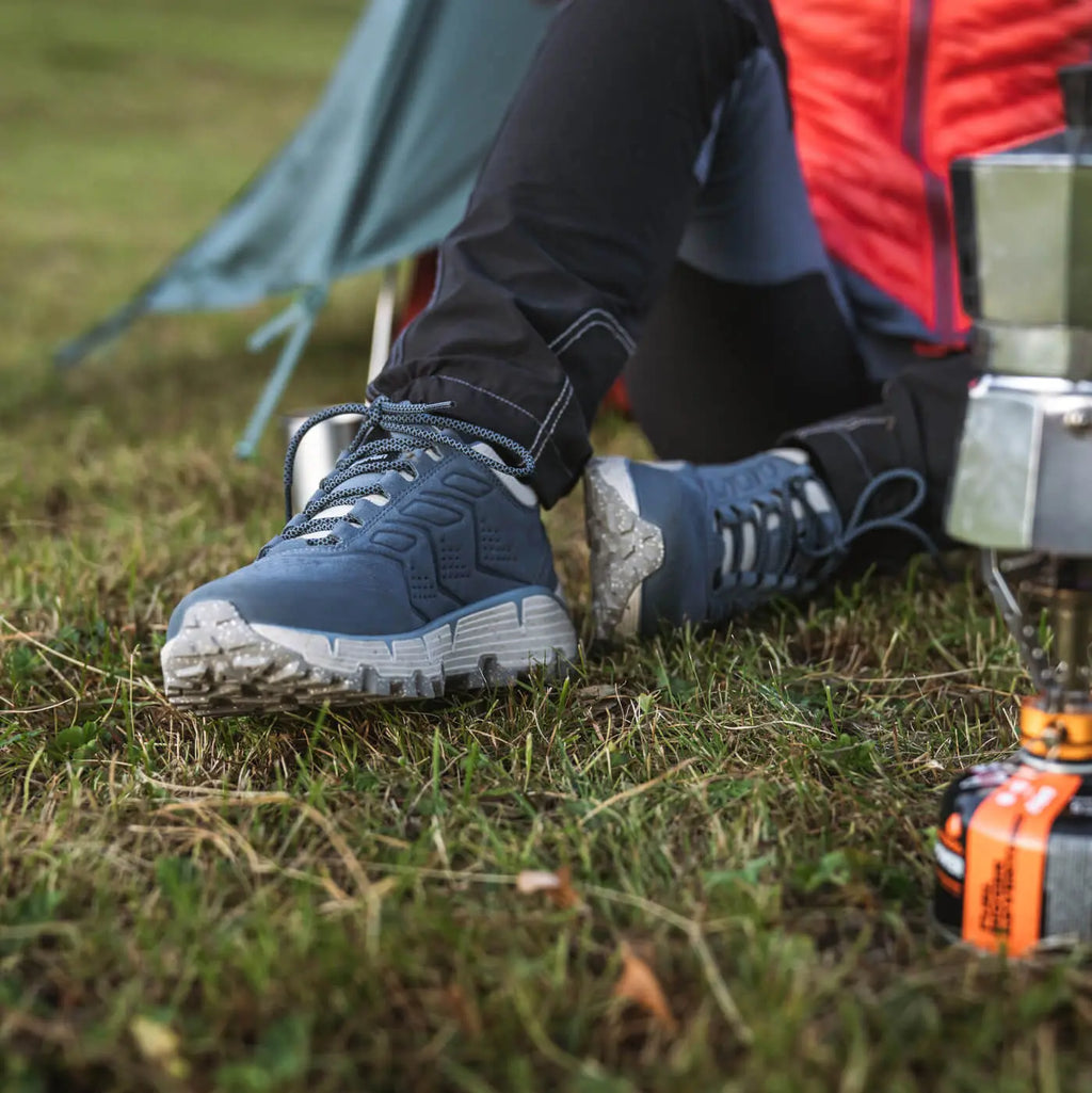 Person wearing blue hiking boots sitting on grass with camping gear around