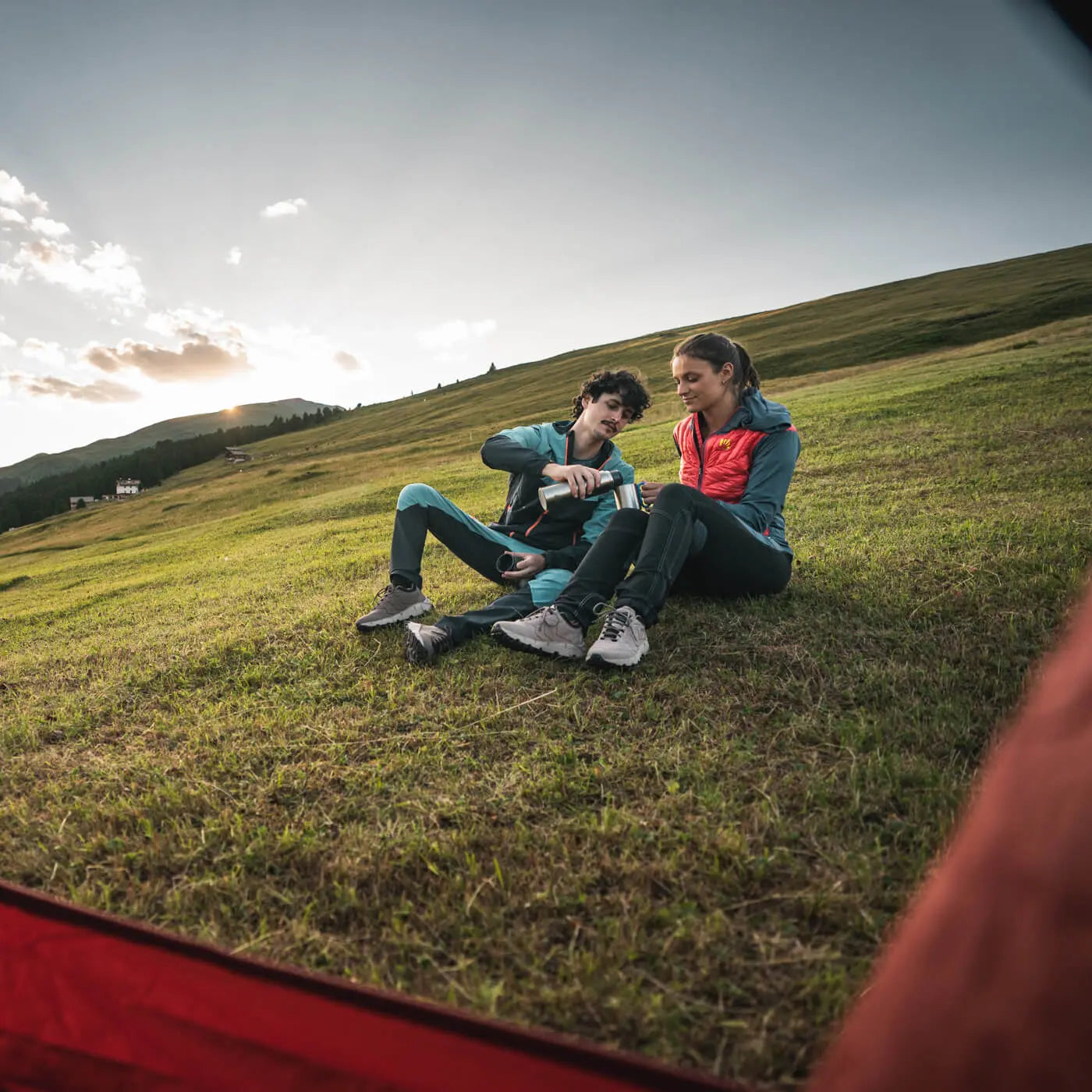 Two people sitting on a grassy hillside with a scenic background
