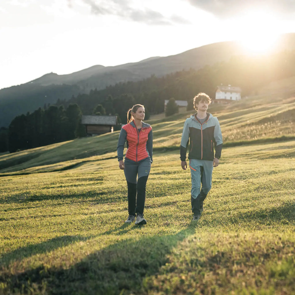 Two people walking on a grassy field with mountains in the background