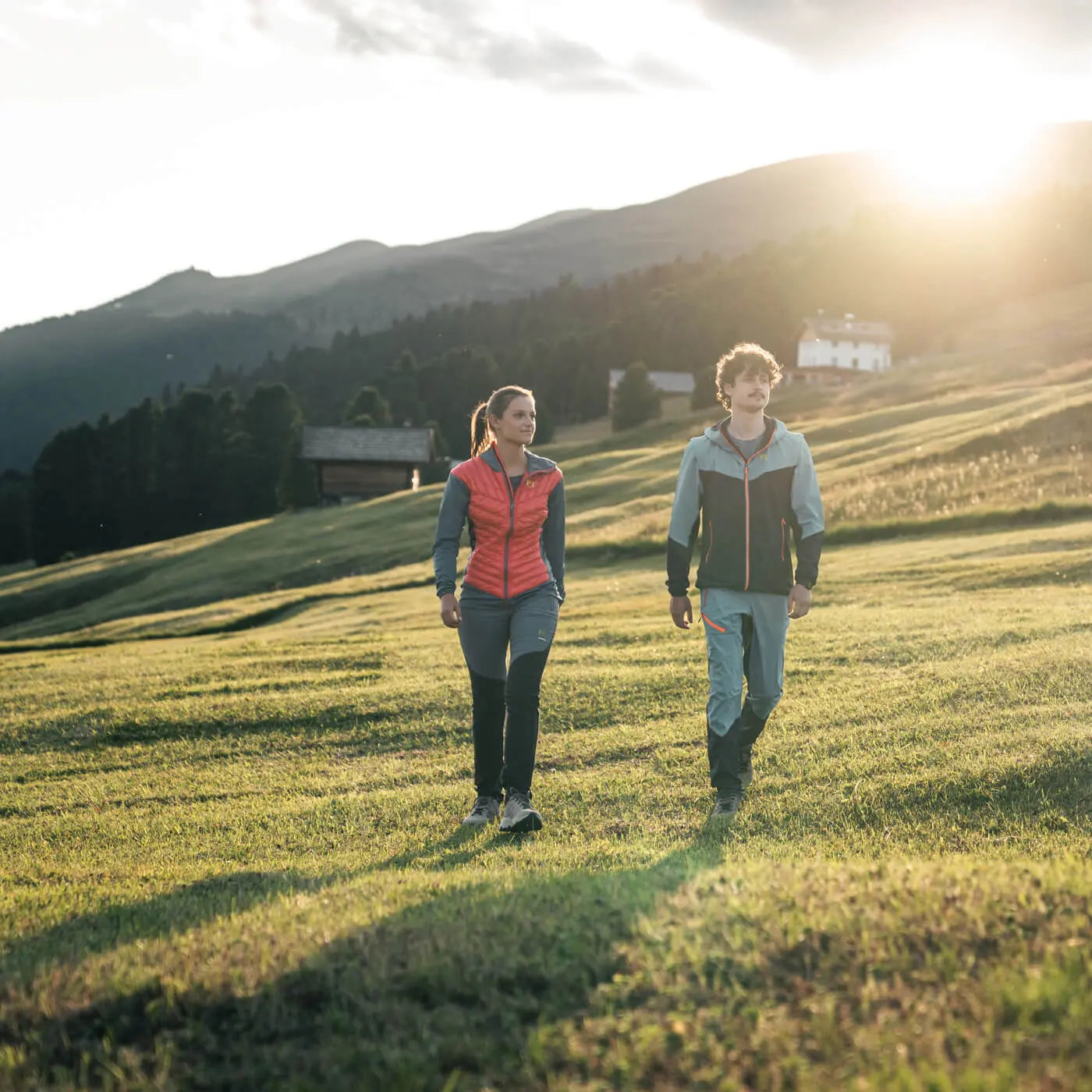 Two people walking on a grassy field with mountains in the background