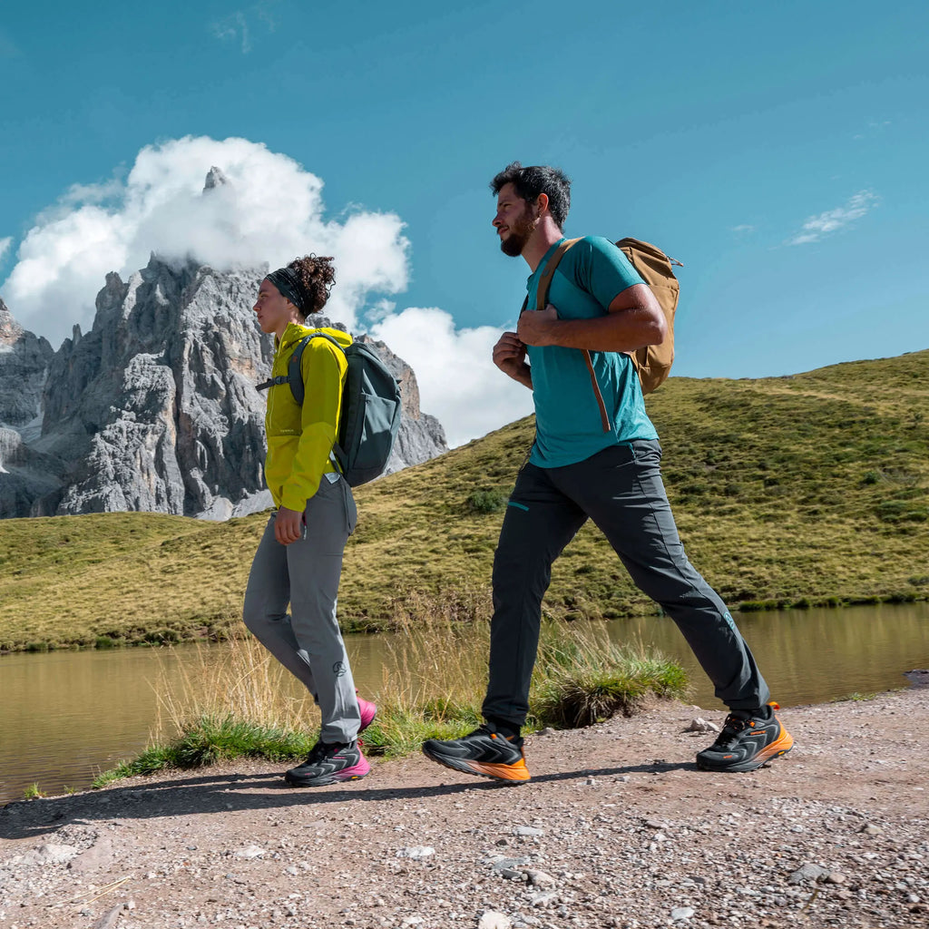 Two hikers walking on a trail with mountains and a lake in the background