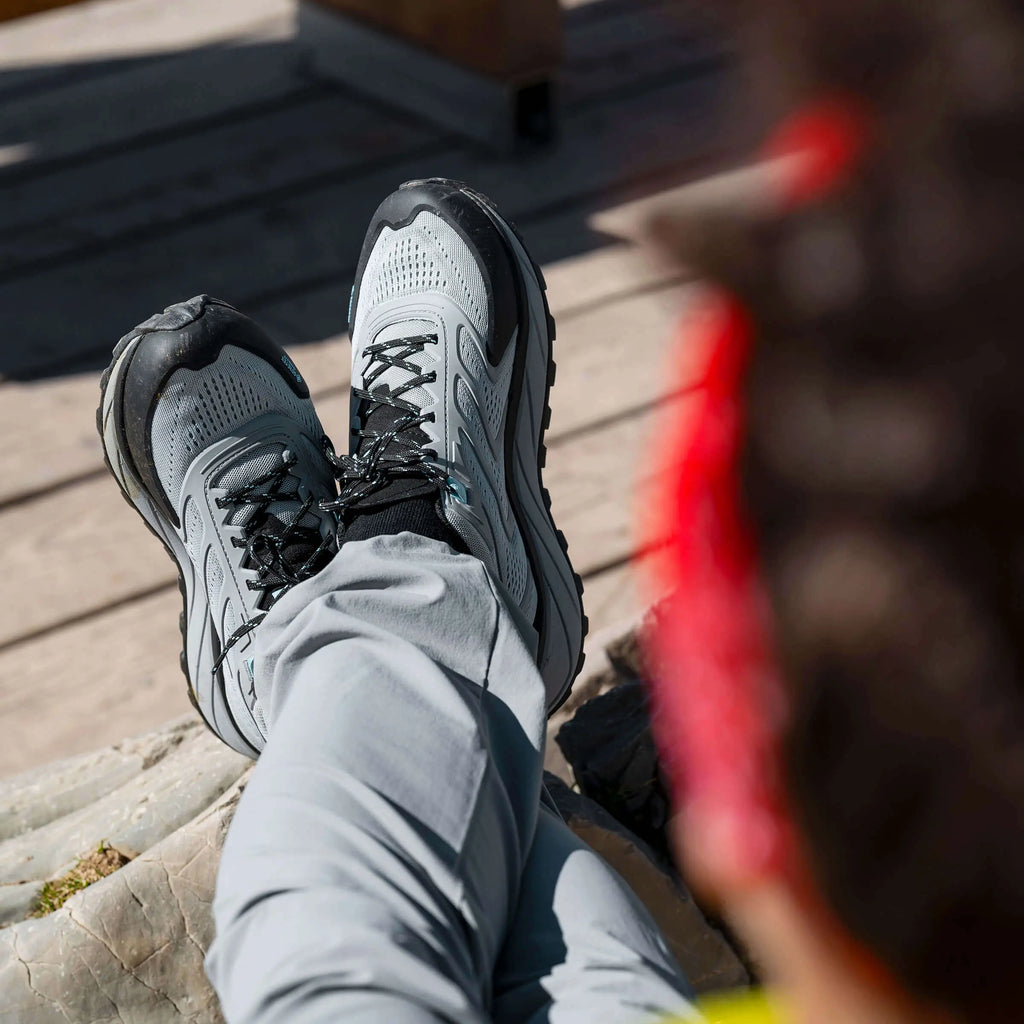 Person wearing gray and black athletic shoes on a wooden deck.