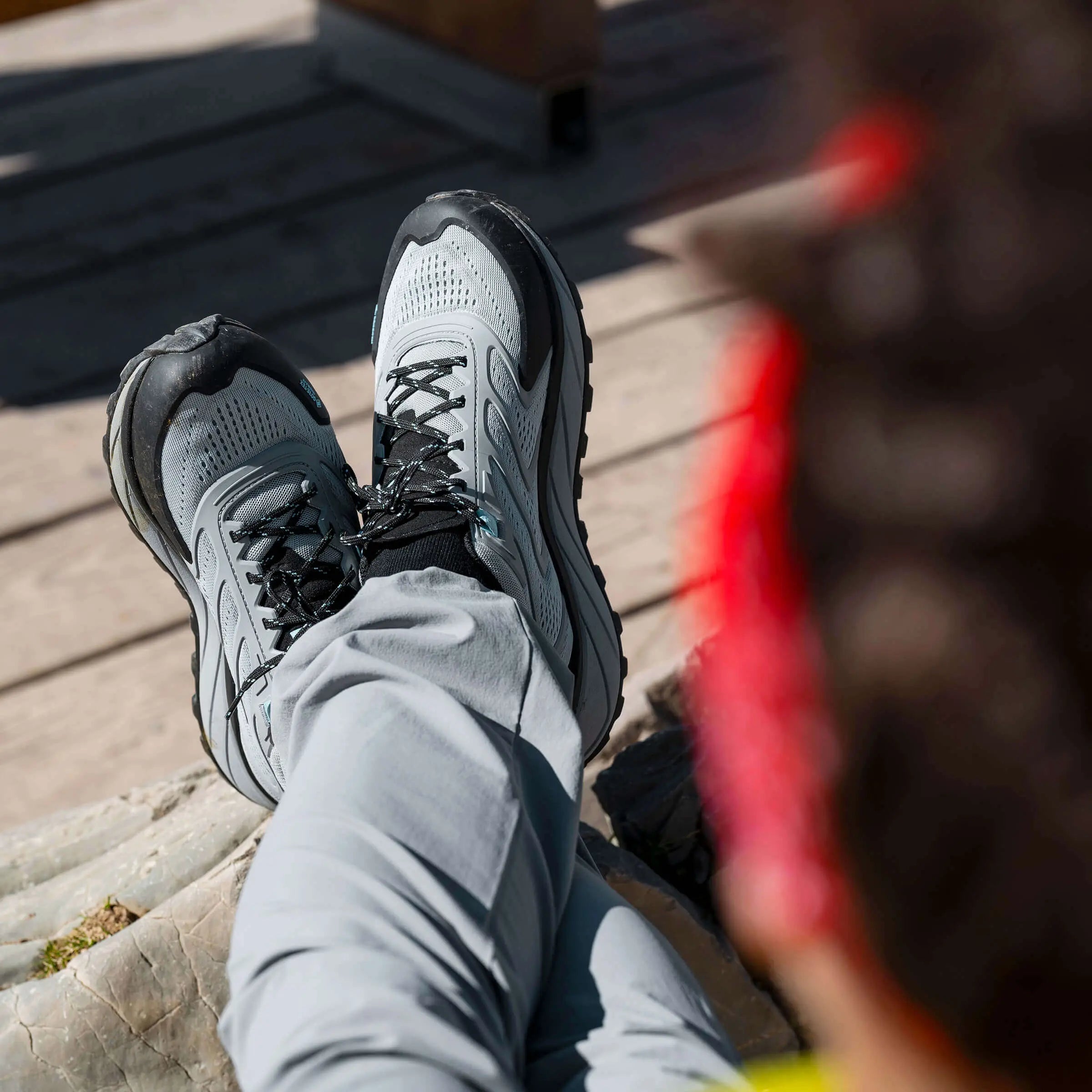 Person wearing gray and black athletic shoes on a wooden deck.