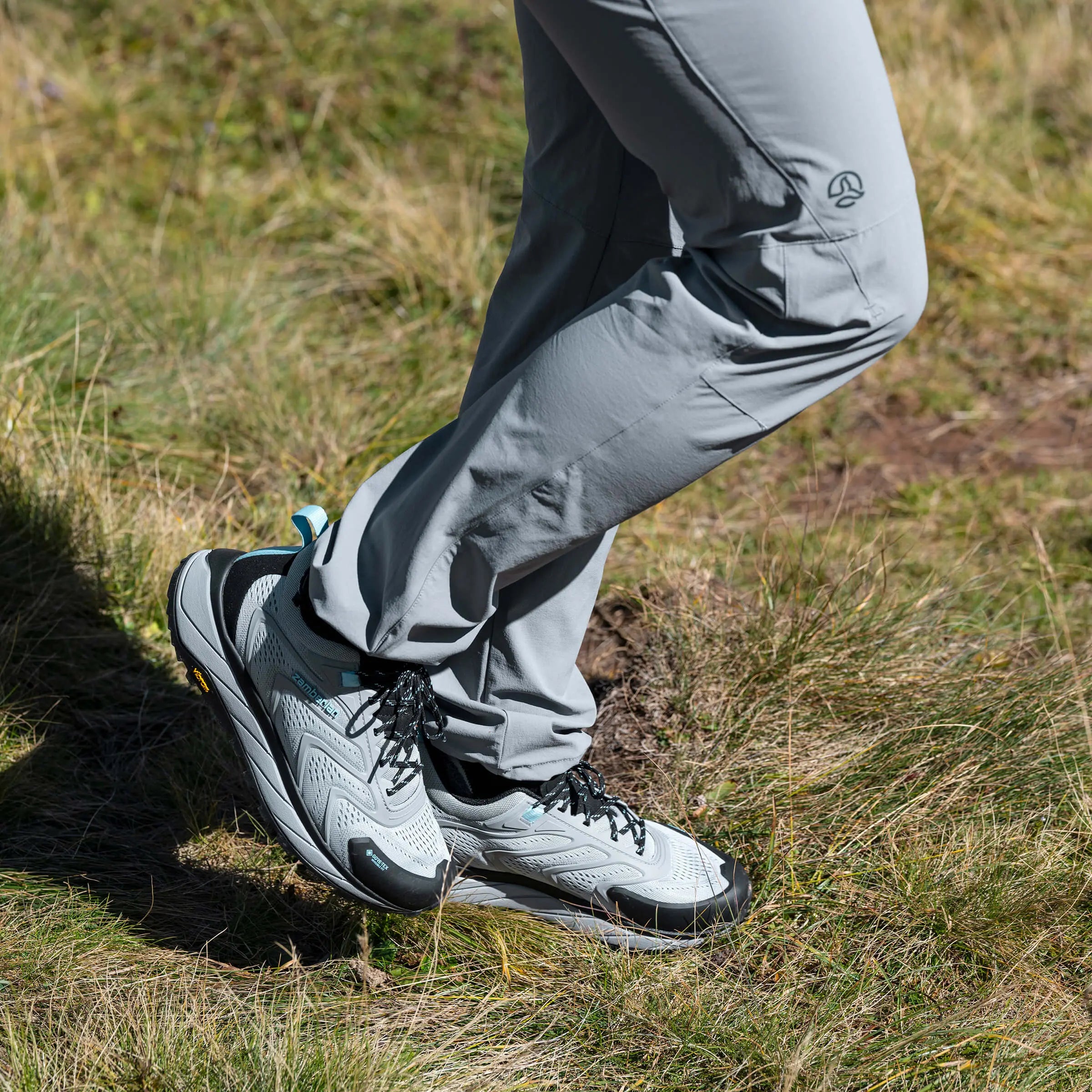 Person wearing gray hiking pants and white hiking shoes on a grassy trail