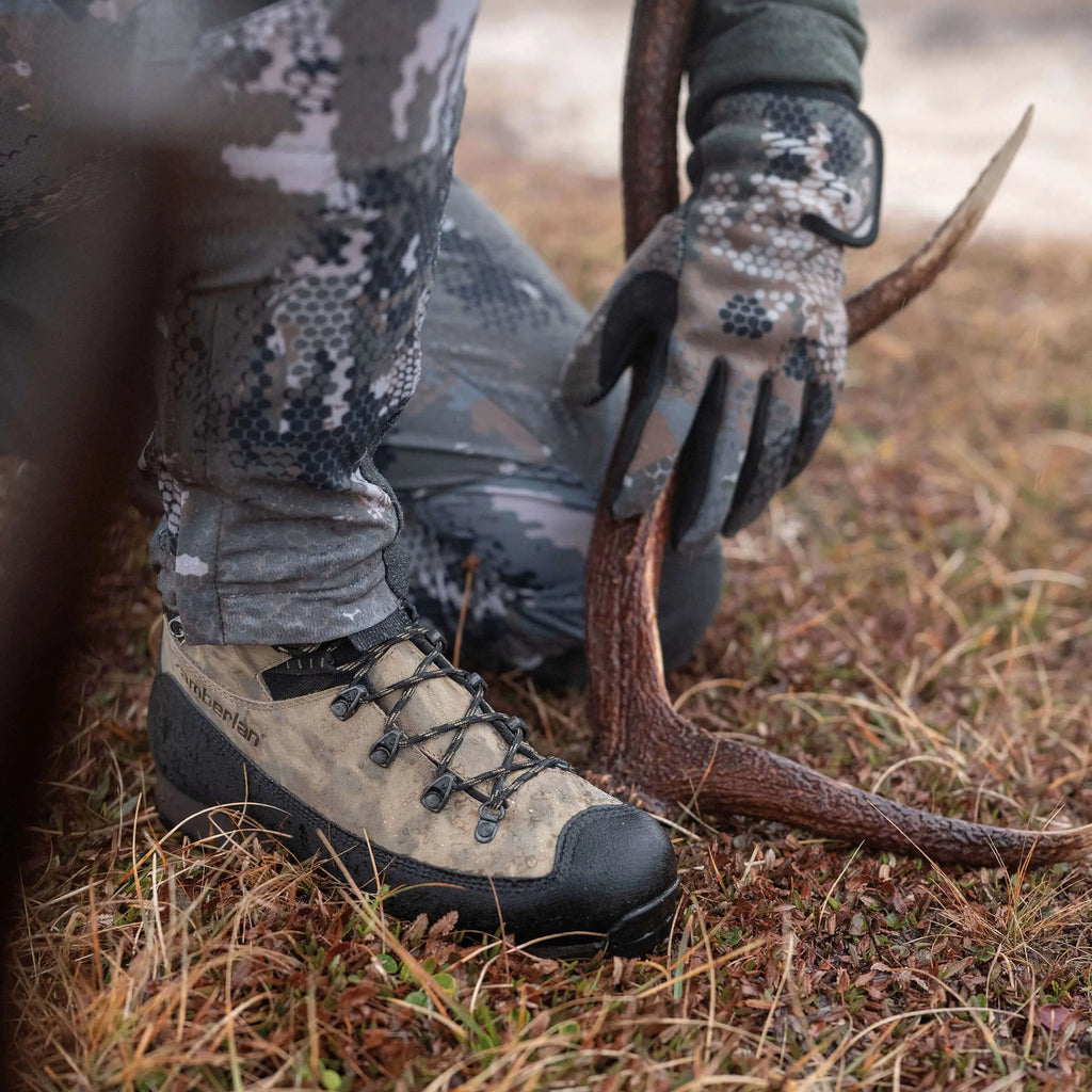 Person in camouflage gear holding a deer antler on a grassy ground
