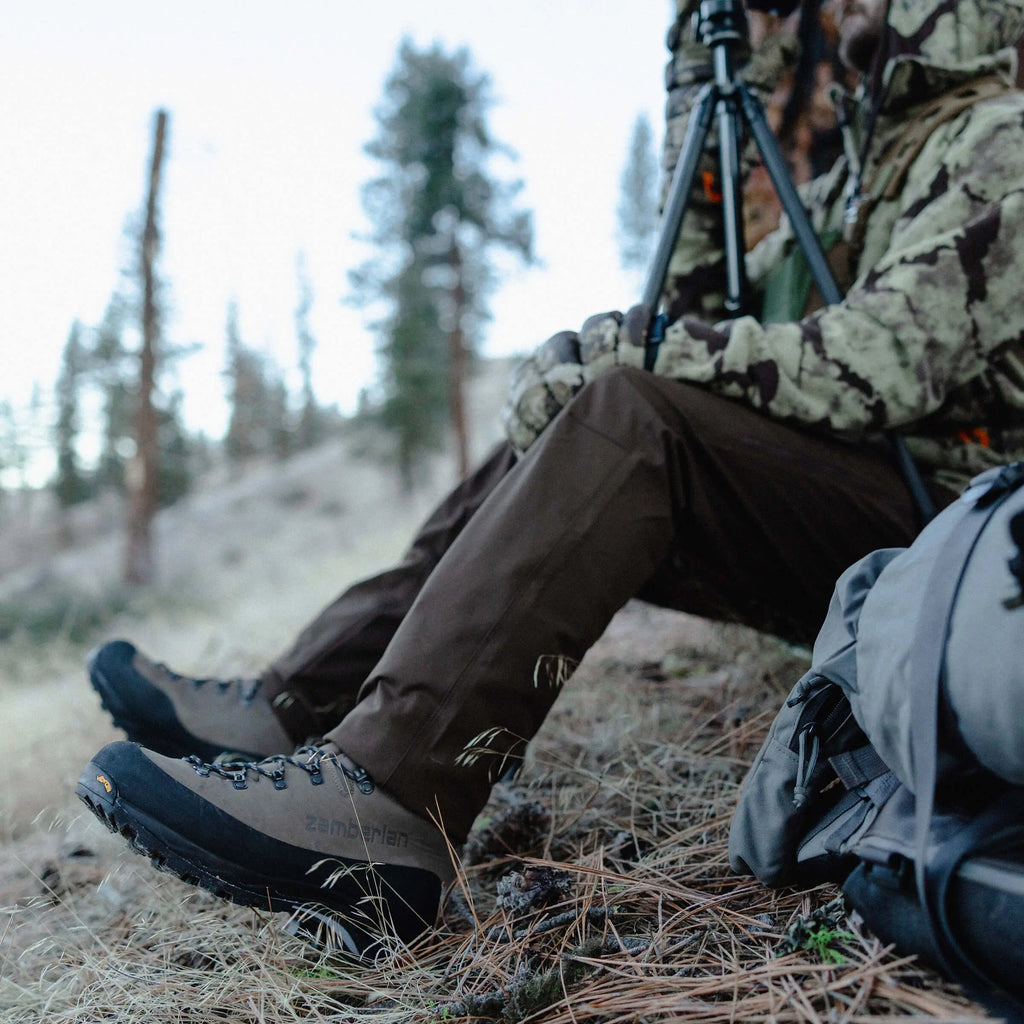 Person in camouflage clothing sitting in a forest with hiking boots on