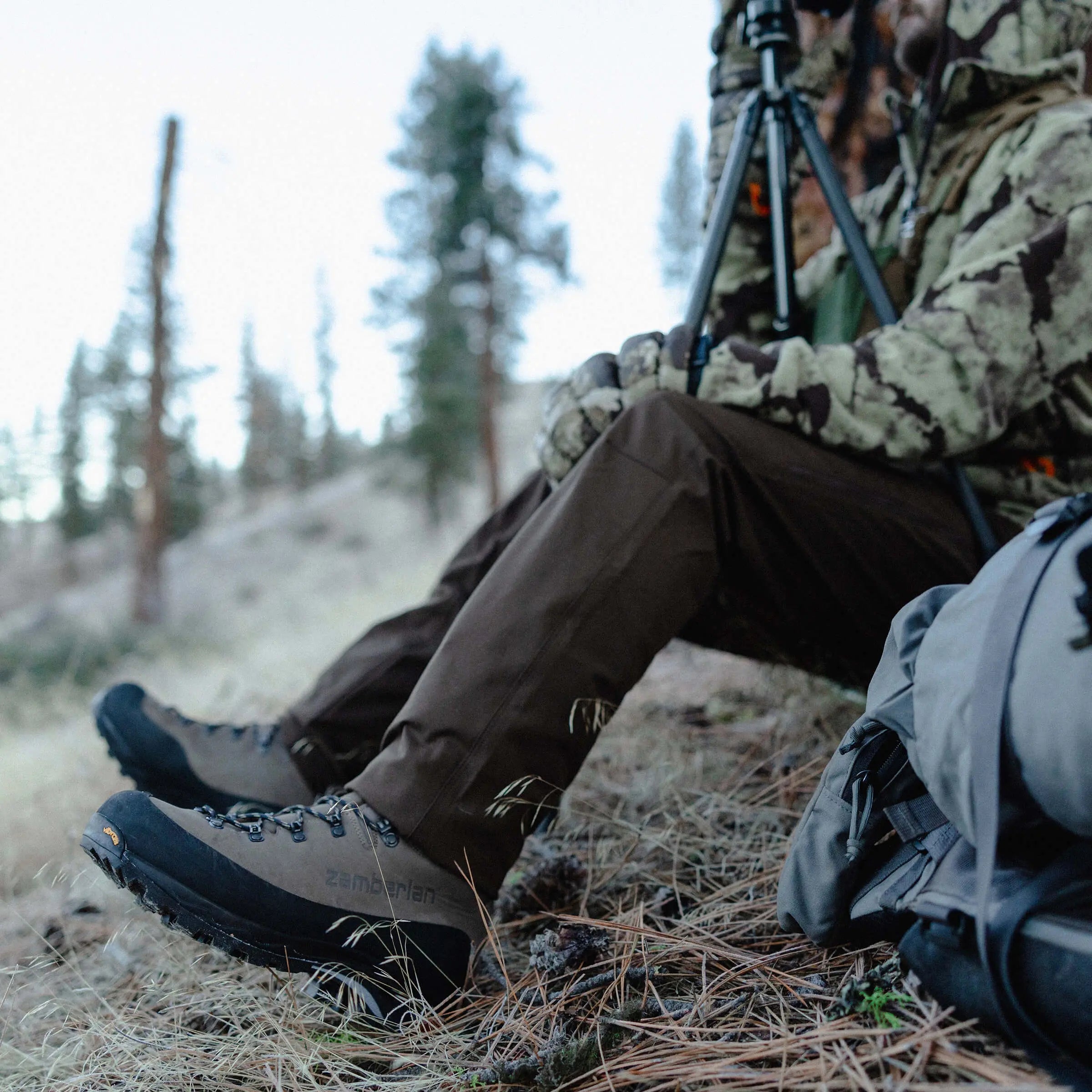 Person in camouflage clothing sitting in a forest with hiking boots on
