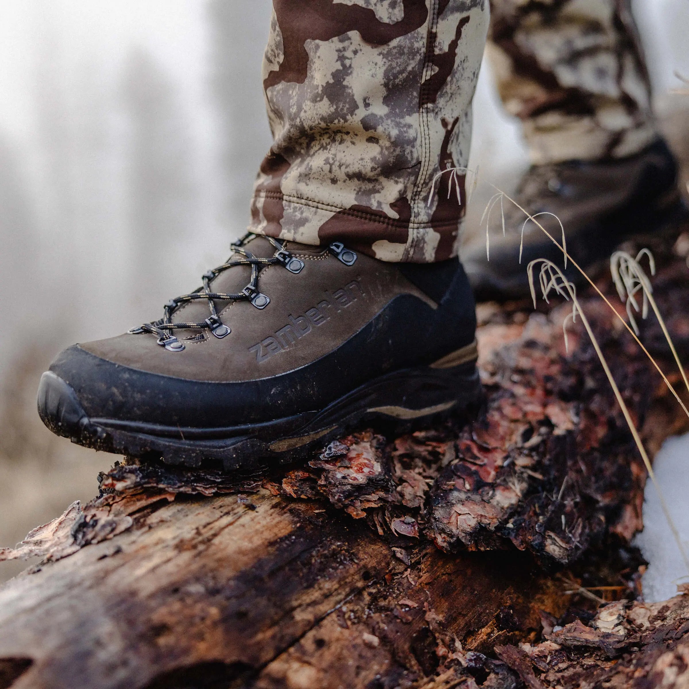 Hiking boot on a log with camouflage pants in a forest setting