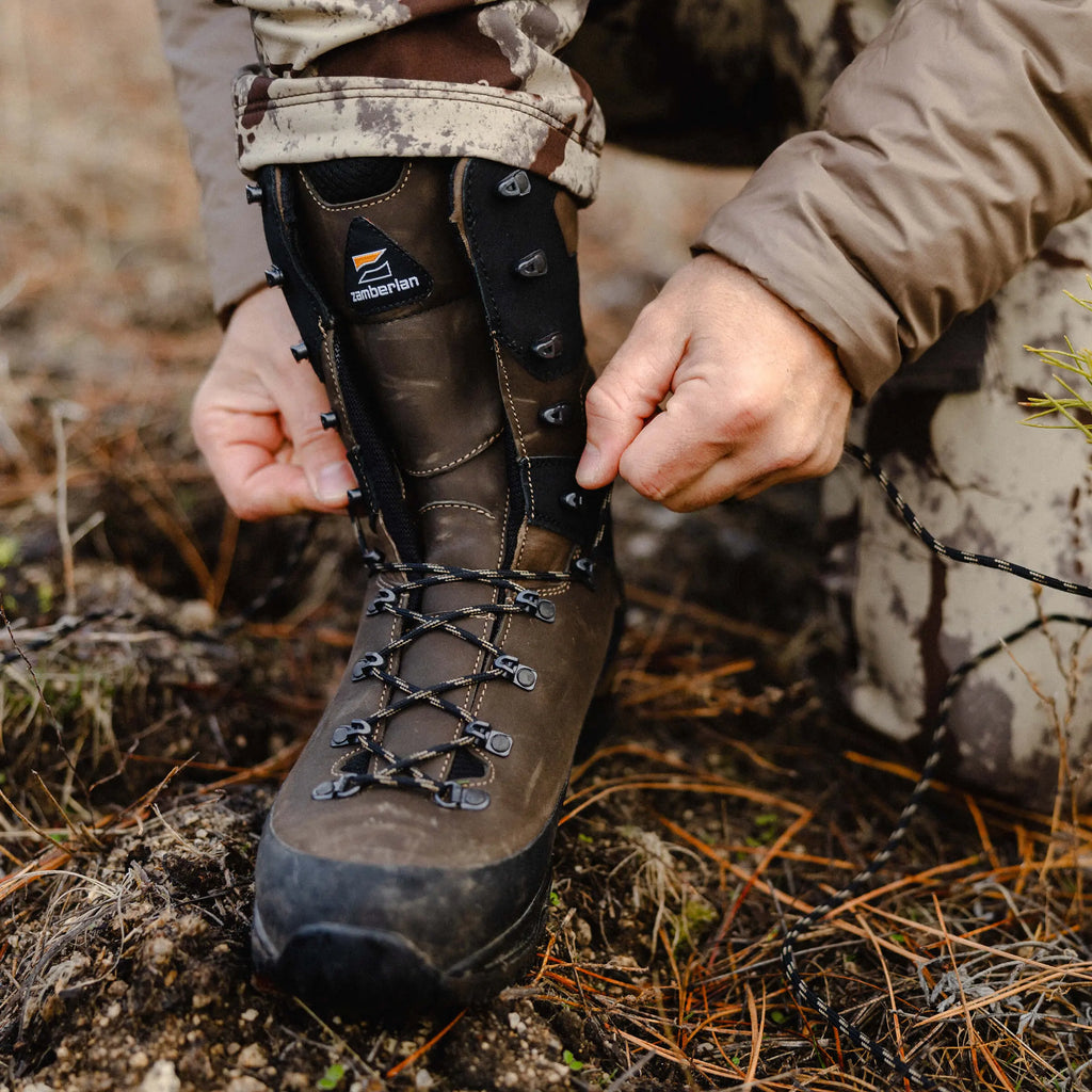 Person adjusting a hiking boot with a brand logo on a natural background