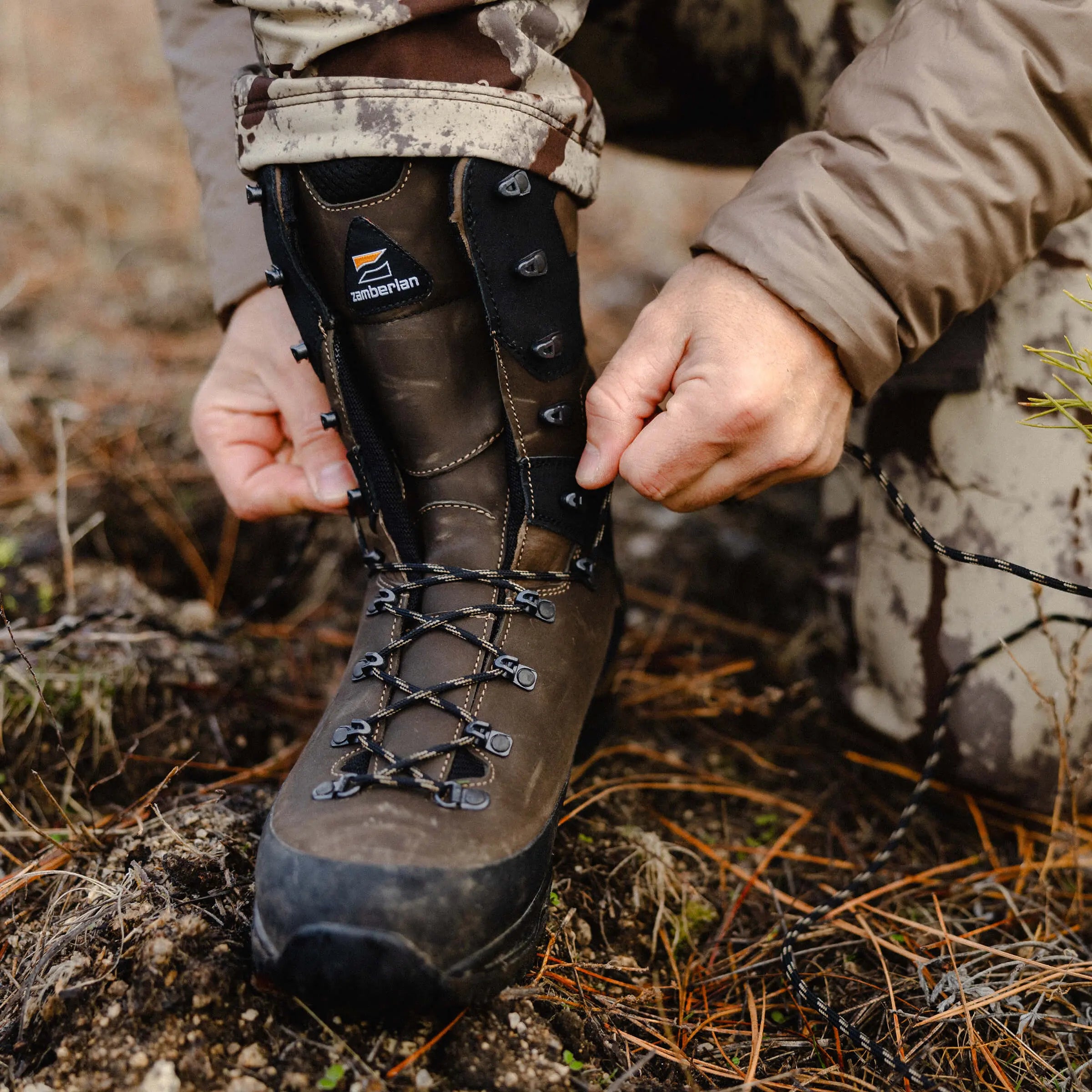 Person adjusting a hiking boot with a brand logo on a natural background