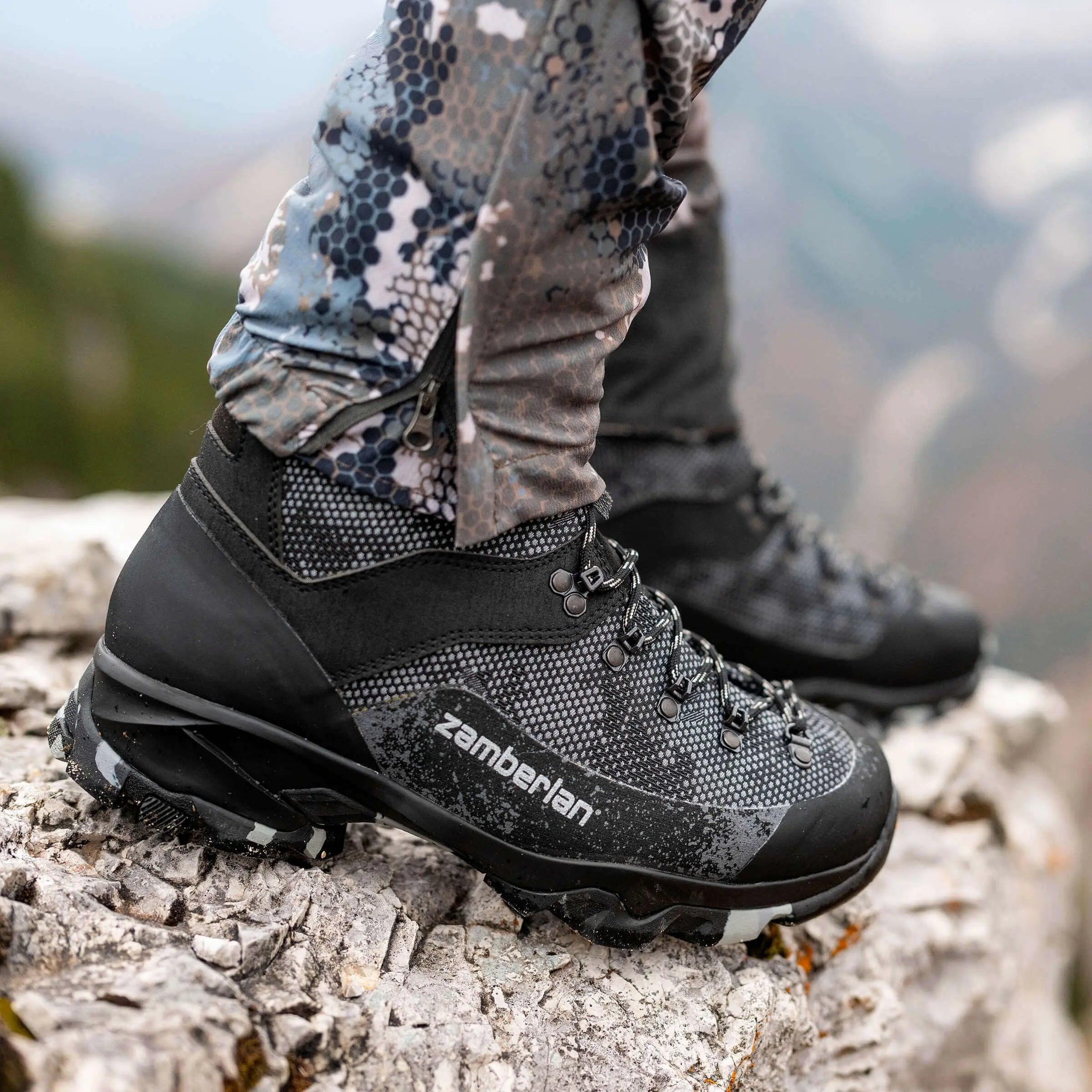 Hiking boots with Zamberlan branding on a rocky surface with a mountainous background.