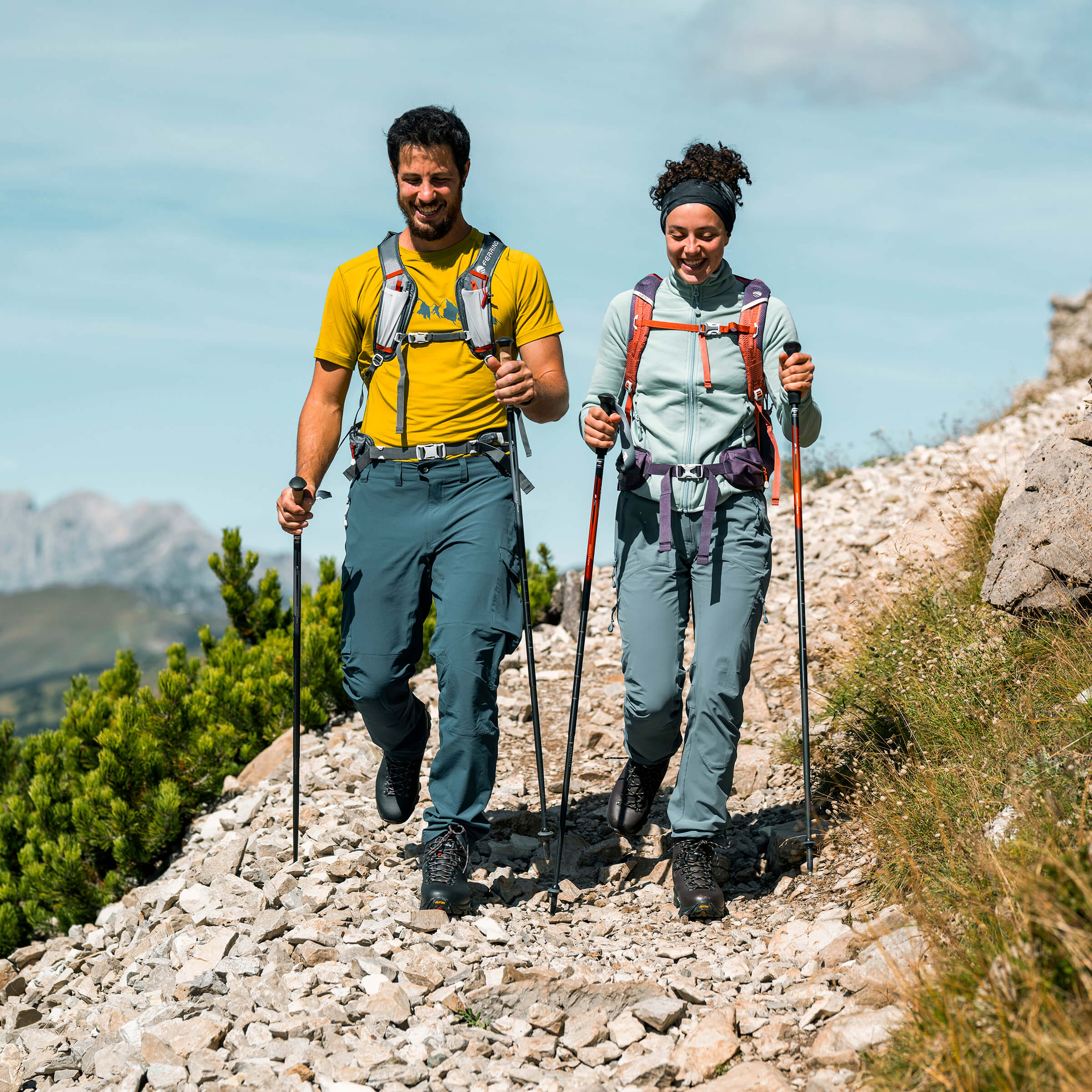 Two hikers on a mountain trail with backpacks and hiking poles.