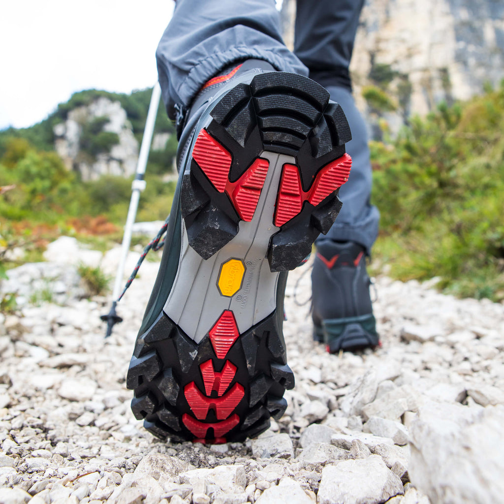 Close-up of hiking shoes with red and black sole on a rocky trail