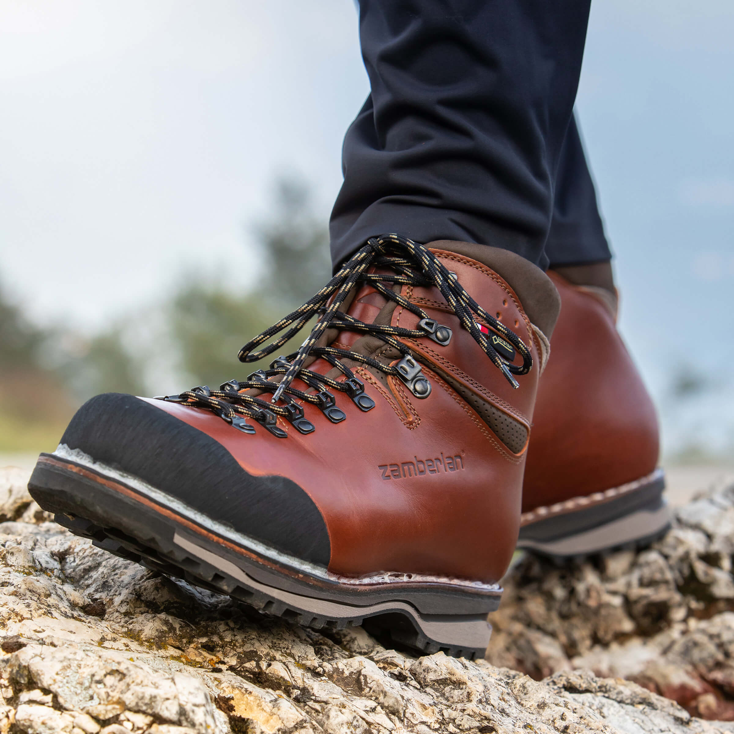 Brown hiking boots with black soles on a rocky surface, brand 'zamberlan' visible.