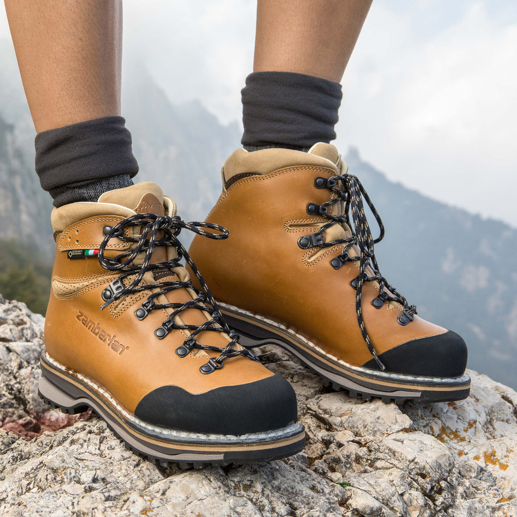 Tan hiking boots with black soles on a rocky surface with a mountainous background