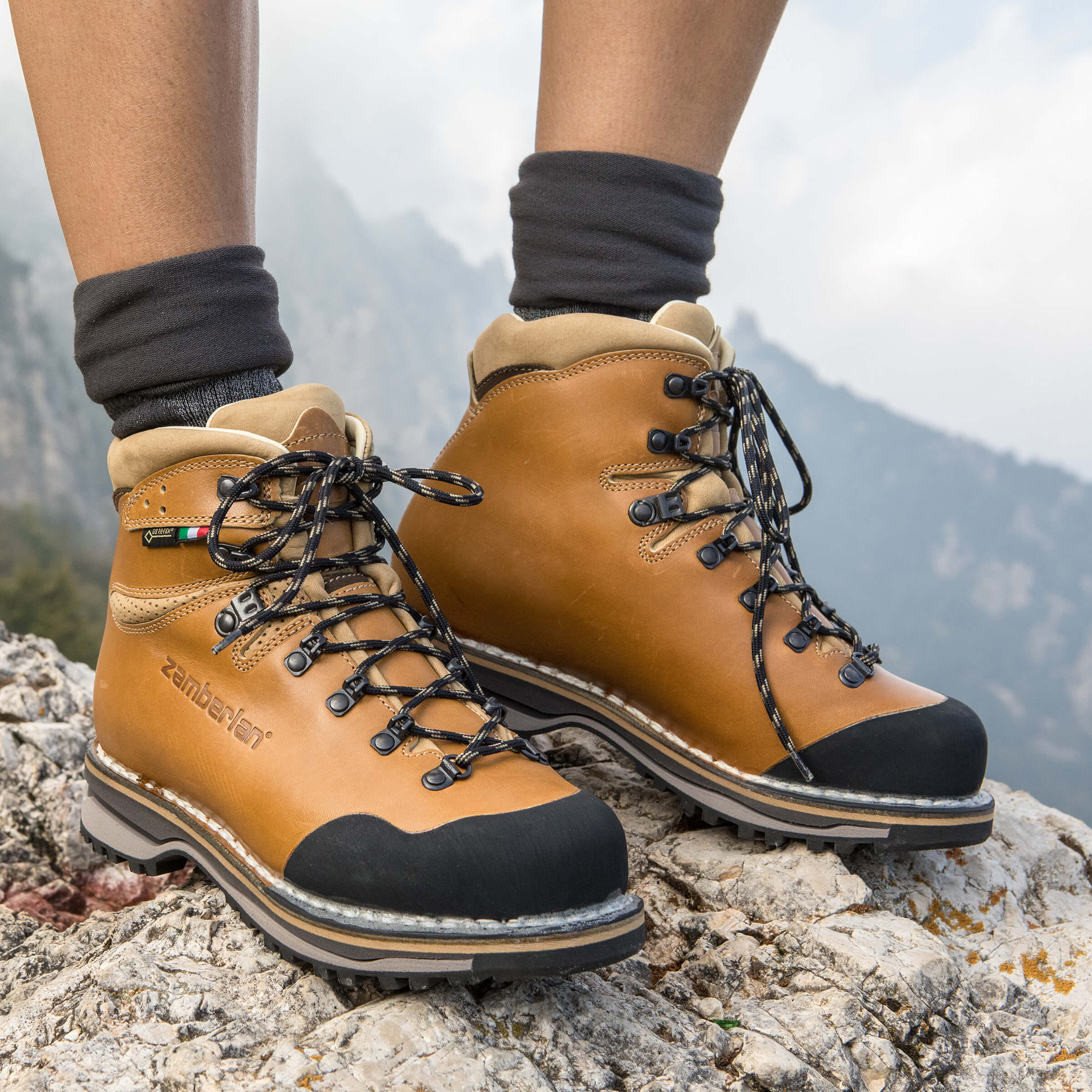 Tan hiking boots with black soles on a rocky surface with a mountainous background