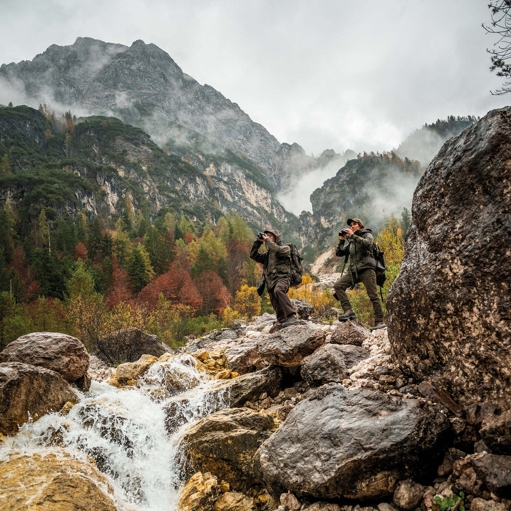 Two hikers on a rocky path with mountains and a waterfall in the background