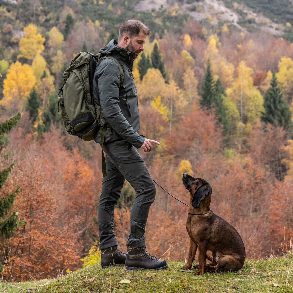 Man with a backpack standing next to a dog in a forest during autumn.