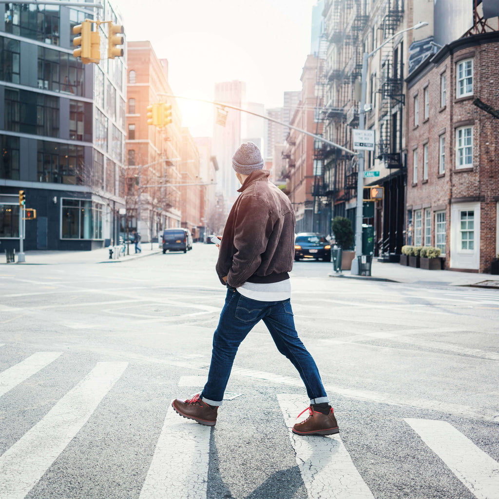 Person crossing a city street with buildings and traffic lights in the background