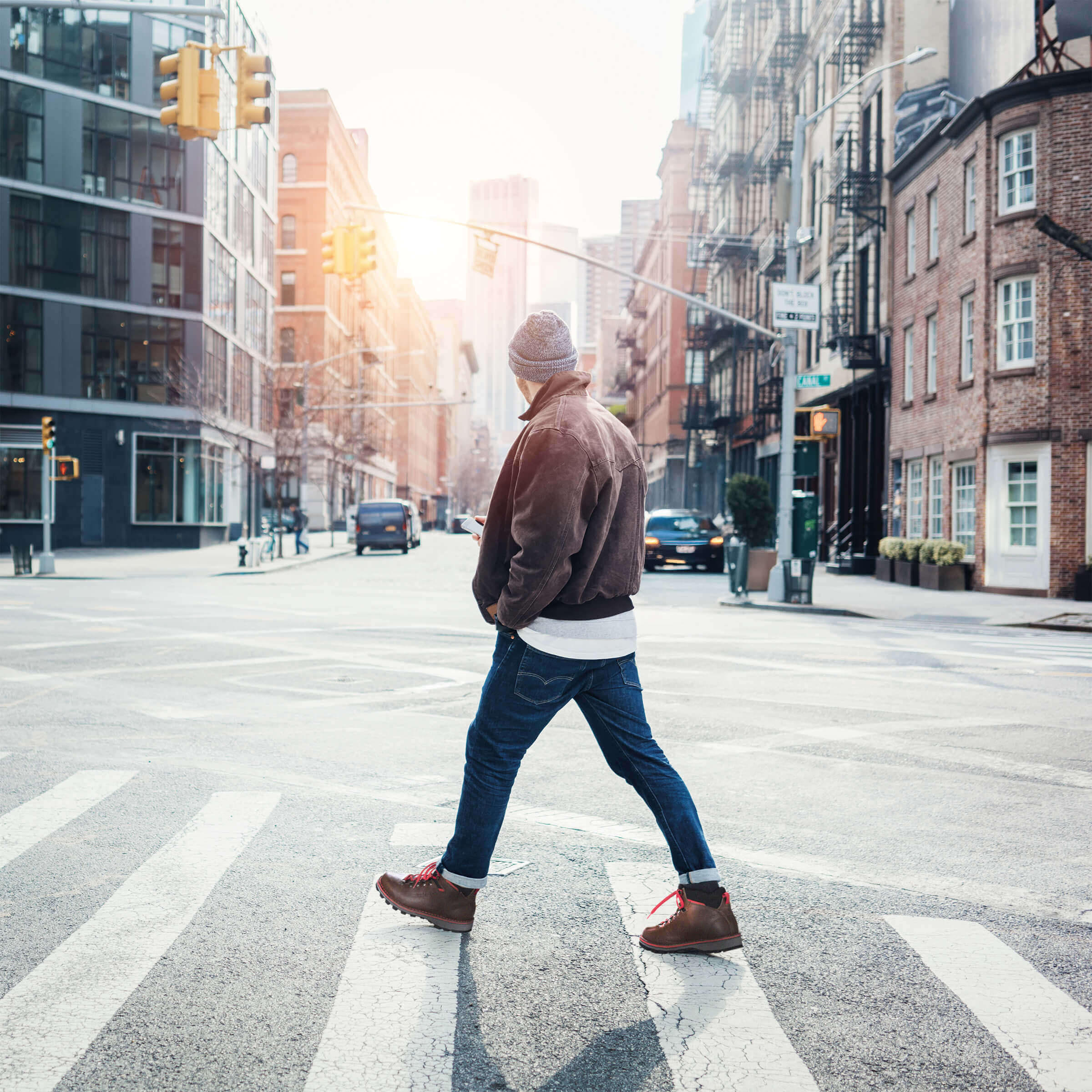 Person crossing a city street with buildings and traffic lights in the background