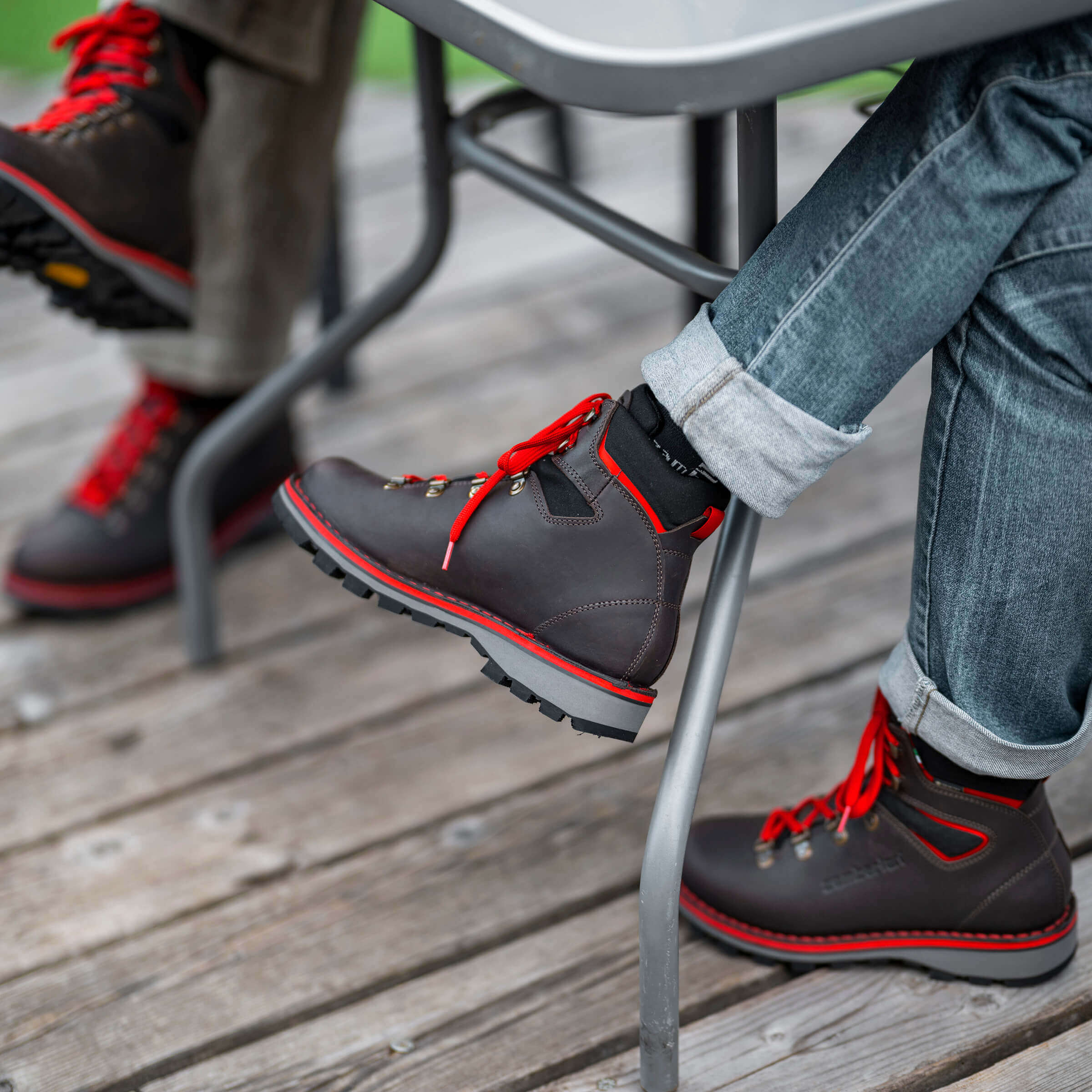 Person wearing black shoes with red laces sitting on a metal chair outdoors.