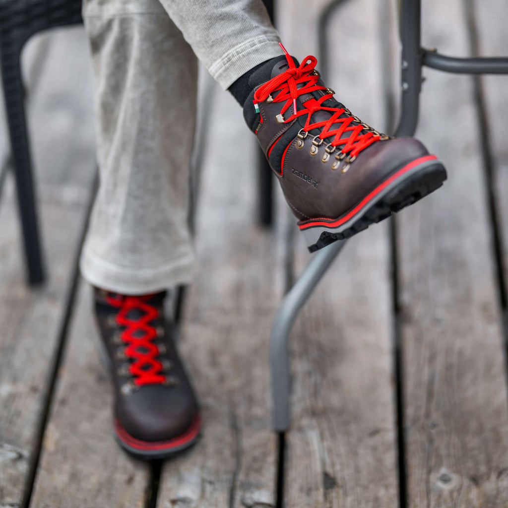 Person wearing brown boots with red laces on a wooden floor.