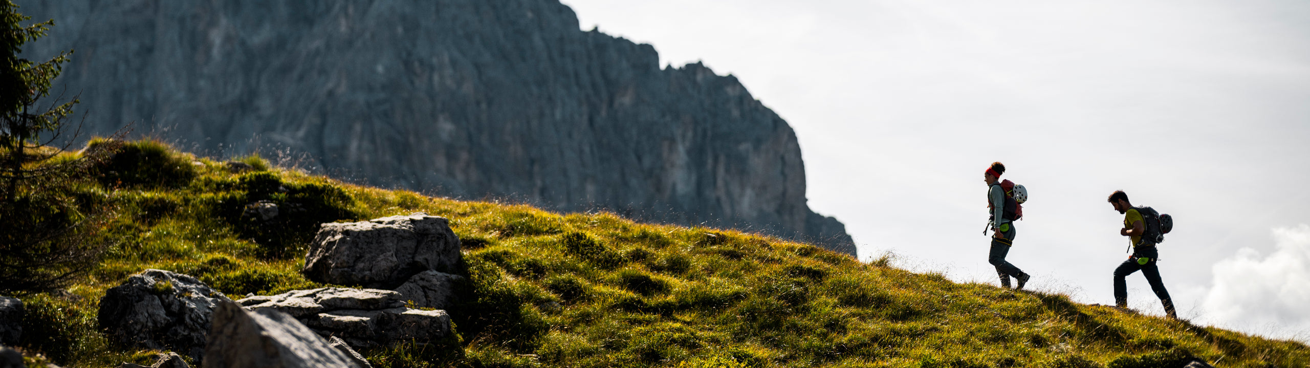 Two hikers on a grassy hill with mountains in the background