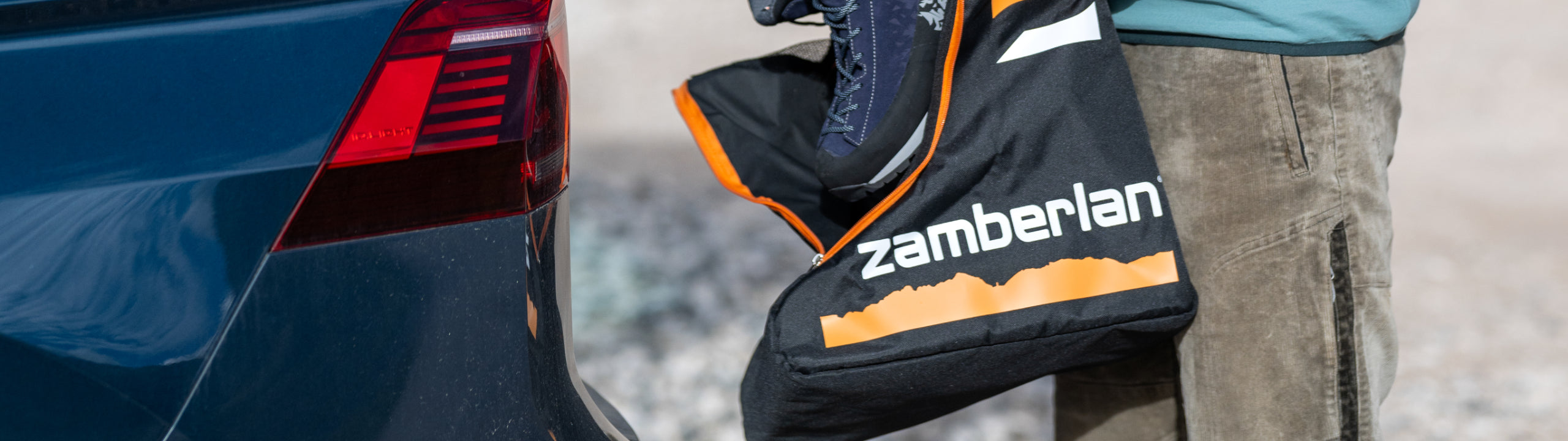 Zamberlan ski boot bag attached to a blue vehicle with a person wearing gray pants in the background.
