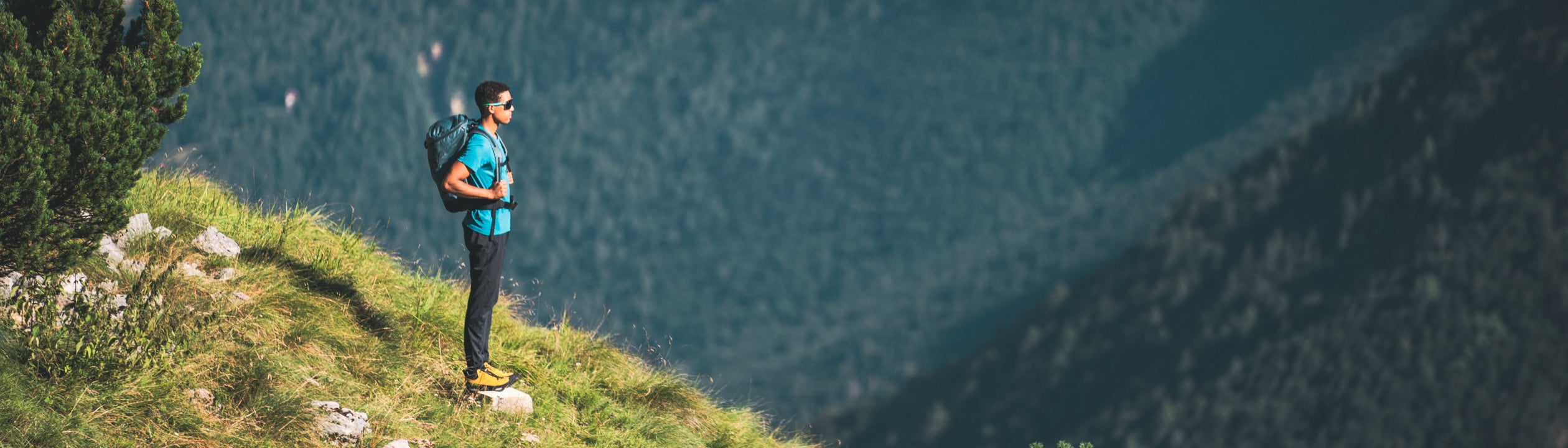 Person standing on a grassy hill with mountains and a lake in the background