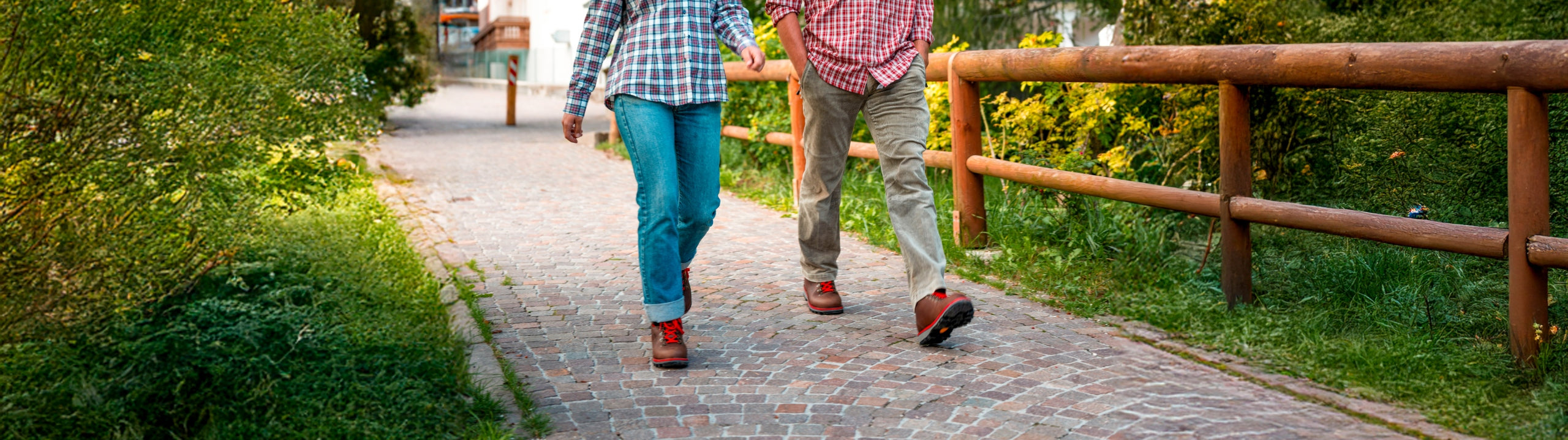 Two people walking hand in hand on a paved path with greenery on either side.