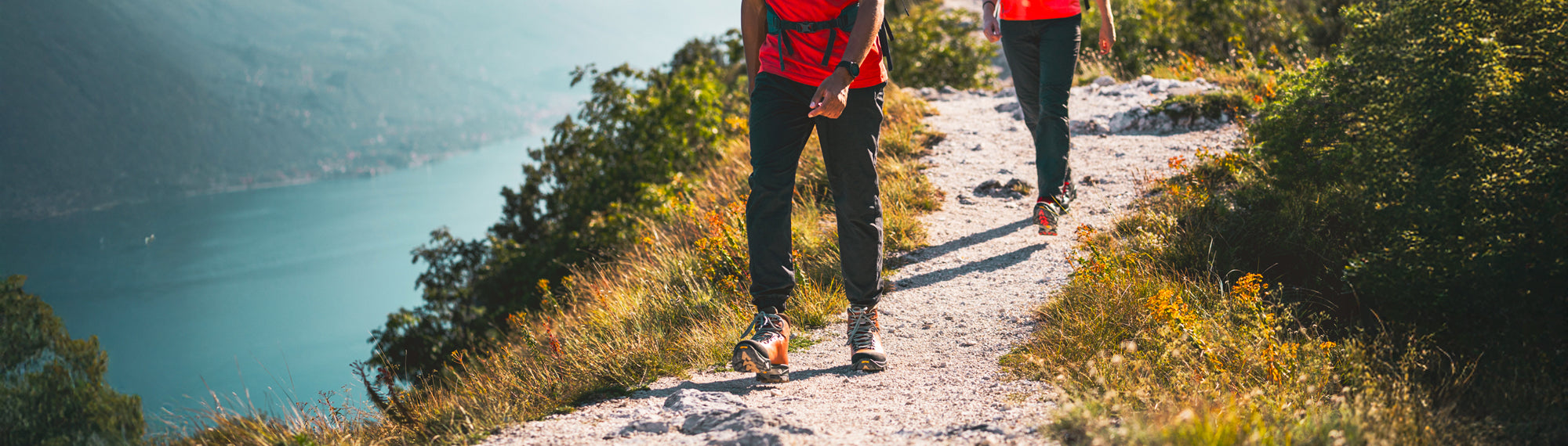 Two people walking on a trail with a scenic view of a lake and mountains.