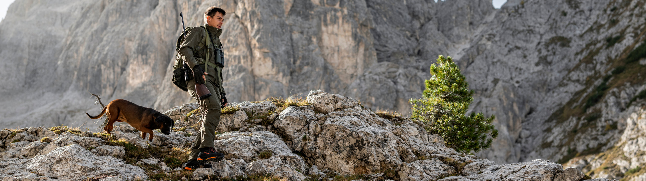 Man with a dog on a rocky mountain peak with mountains in the background