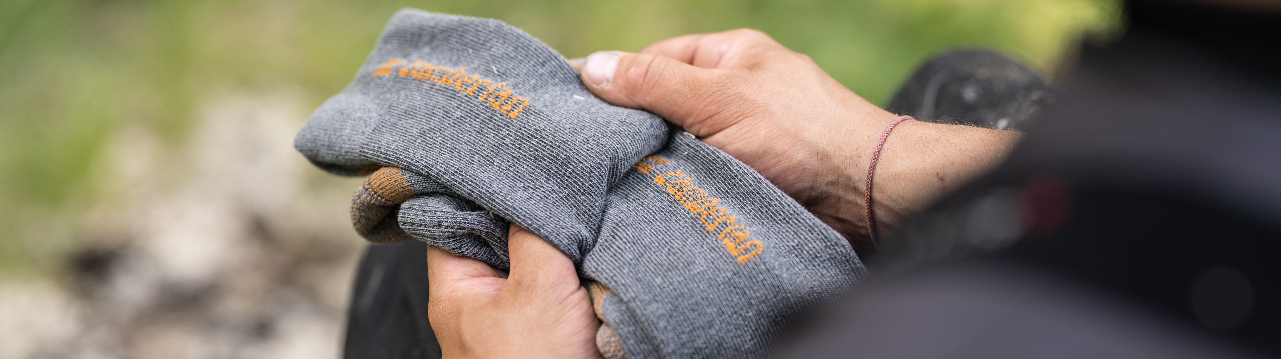 Person holding a gray sock with branding in an outdoor setting