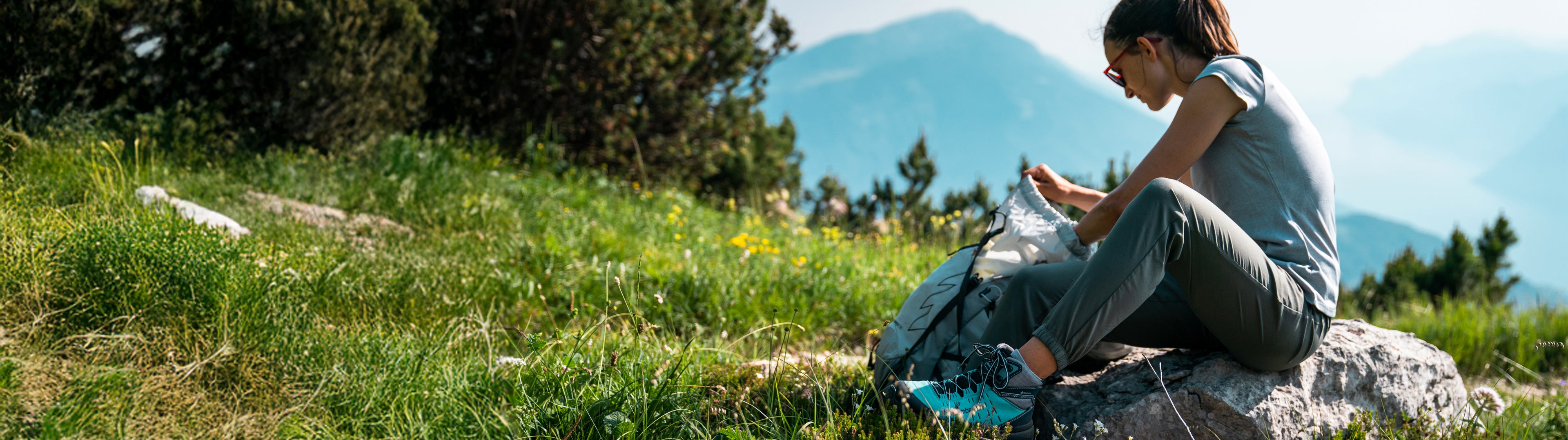 Person sitting on a rock in a grassy field with mountains in the background
