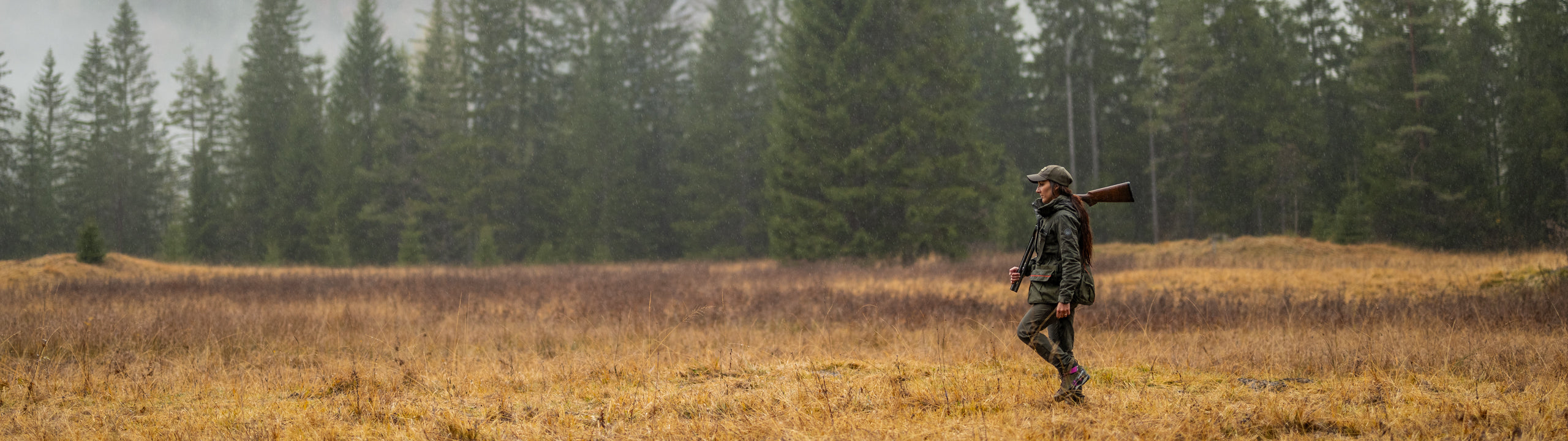 Hunter walking through a field with trees in the background