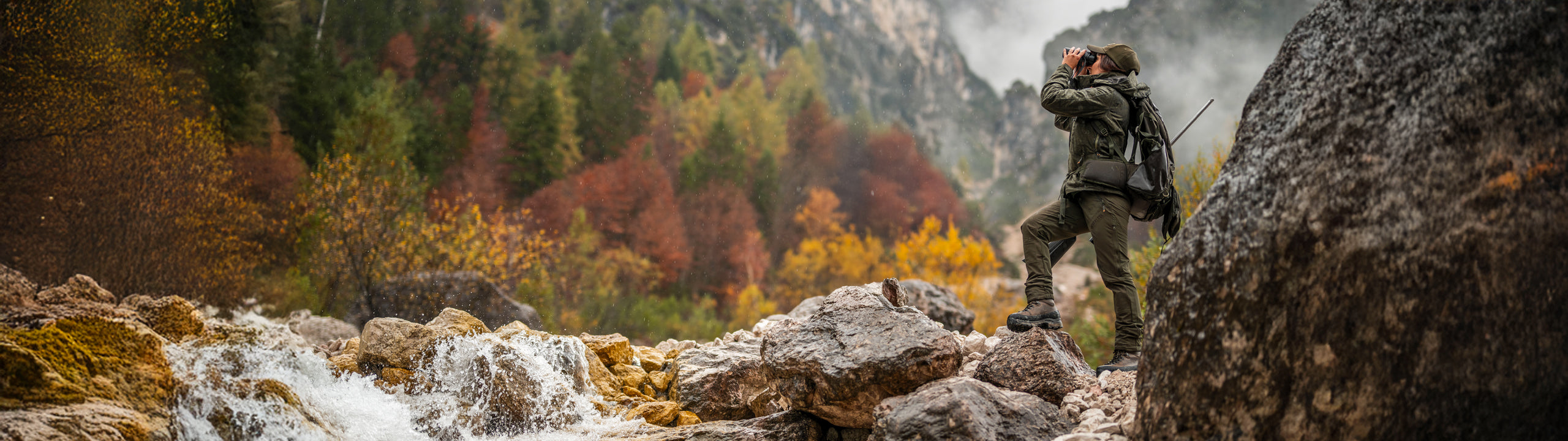 Hunter hiking through a mountainous forest with a waterfall in the background