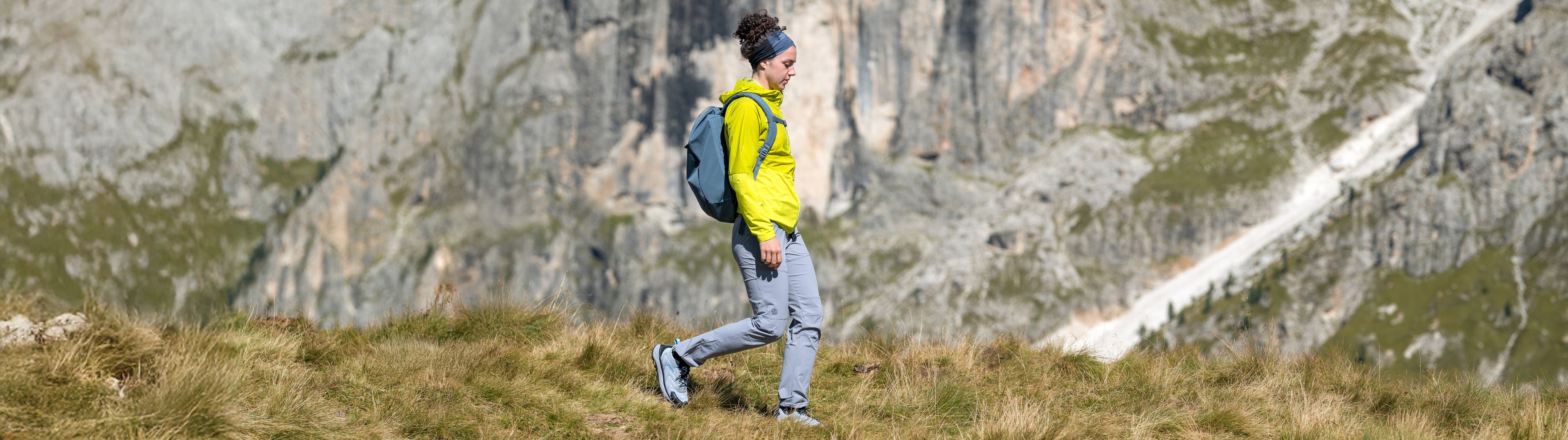 Person hiking in a mountainous area with a backpack and yellow jacket.